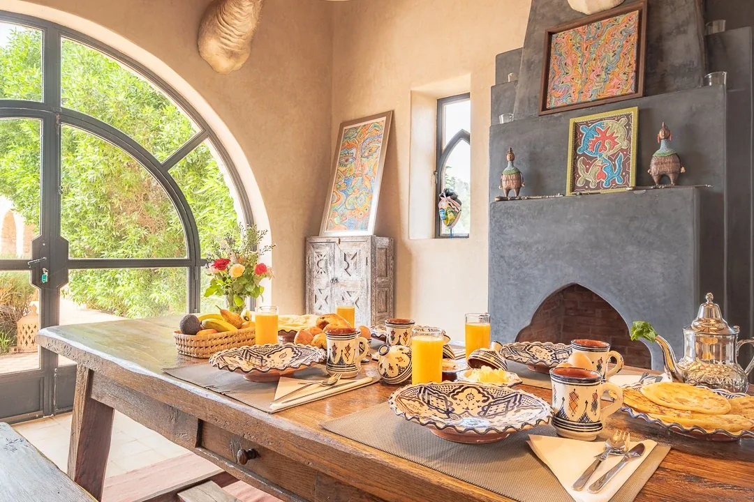 Table en bois dressée pour le petit-déjeuner près d'une cheminée et d'une fenêtre en ogive