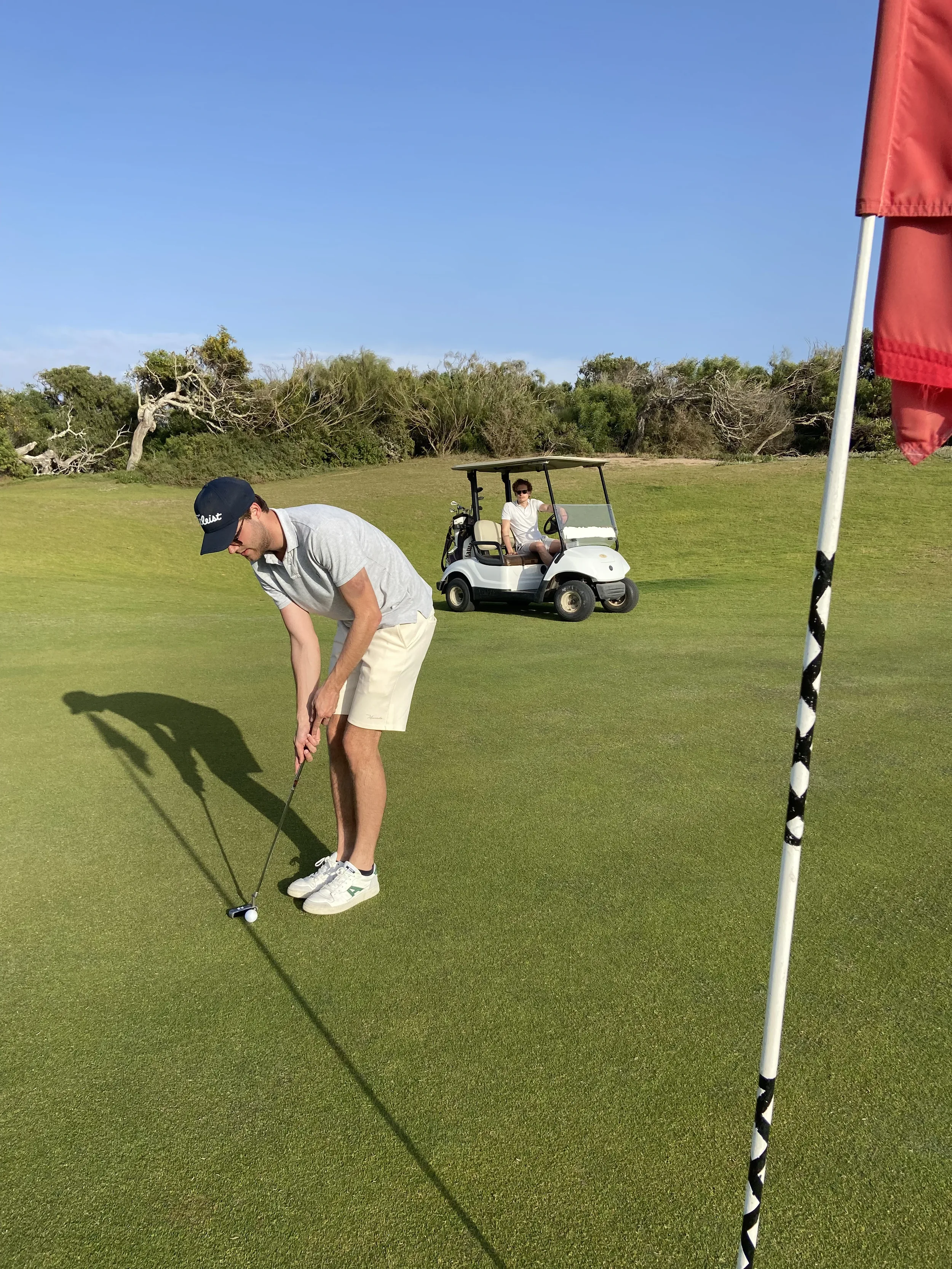 Golfeur en plein putting sur le green, voiturette et drapeau rouge à proximité, parcours près d'Essaouira