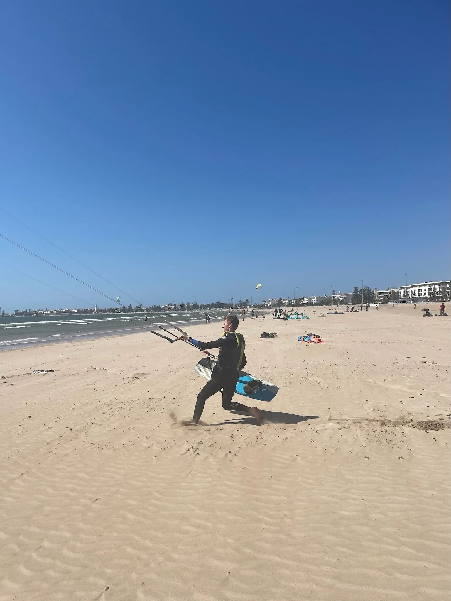 Kitesurfeur courant sur la plage avec sa planche, front de mer d'Essaouira en arrière-plan