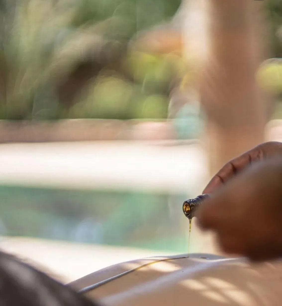 Huile de massage versée délicatement sur le corps lors d'un soin bien-être en bord de piscine