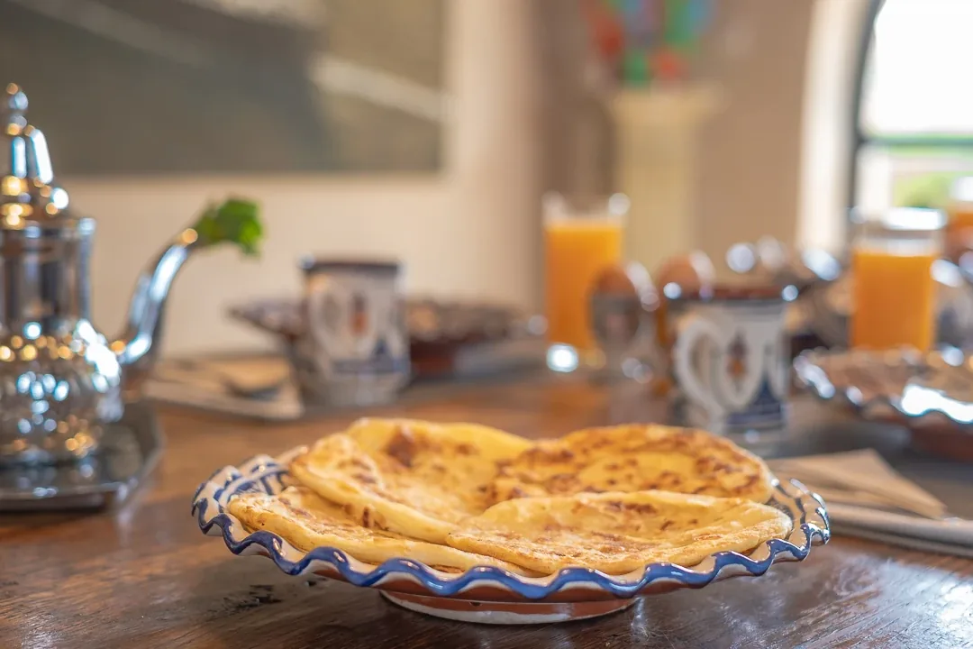 Crêpes marocaines msemen servies sur une assiette à côté d'une théière en argent et de thé à la menthe