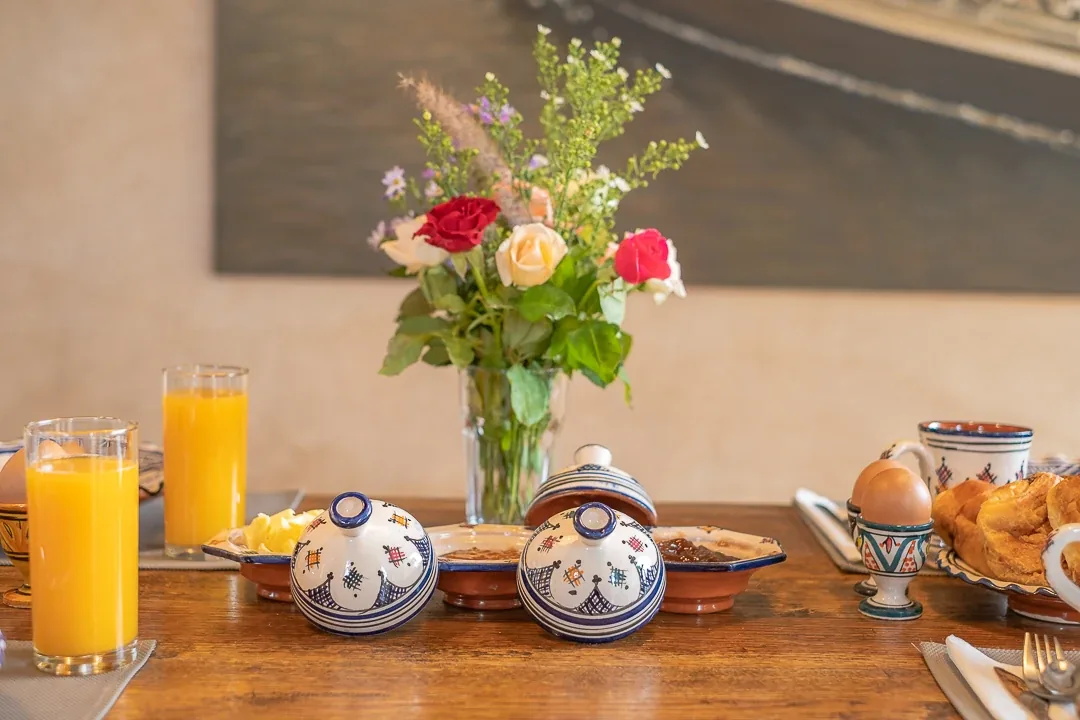 Petit-déjeuner avec bouquet de roses, confitures maison, œufs, viennoiseries et jus d'orange