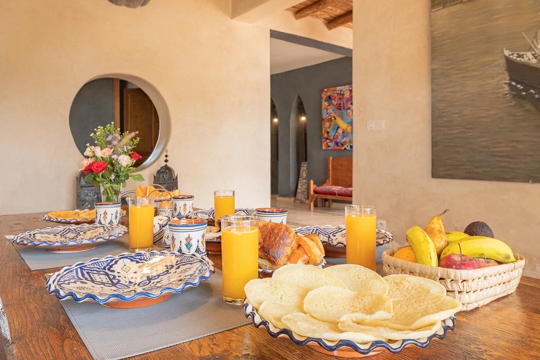Petit-déjeuner avec jus d'orange frais, crêpes marocaines, corbeille de fruits et miroir rond en arrière-plan