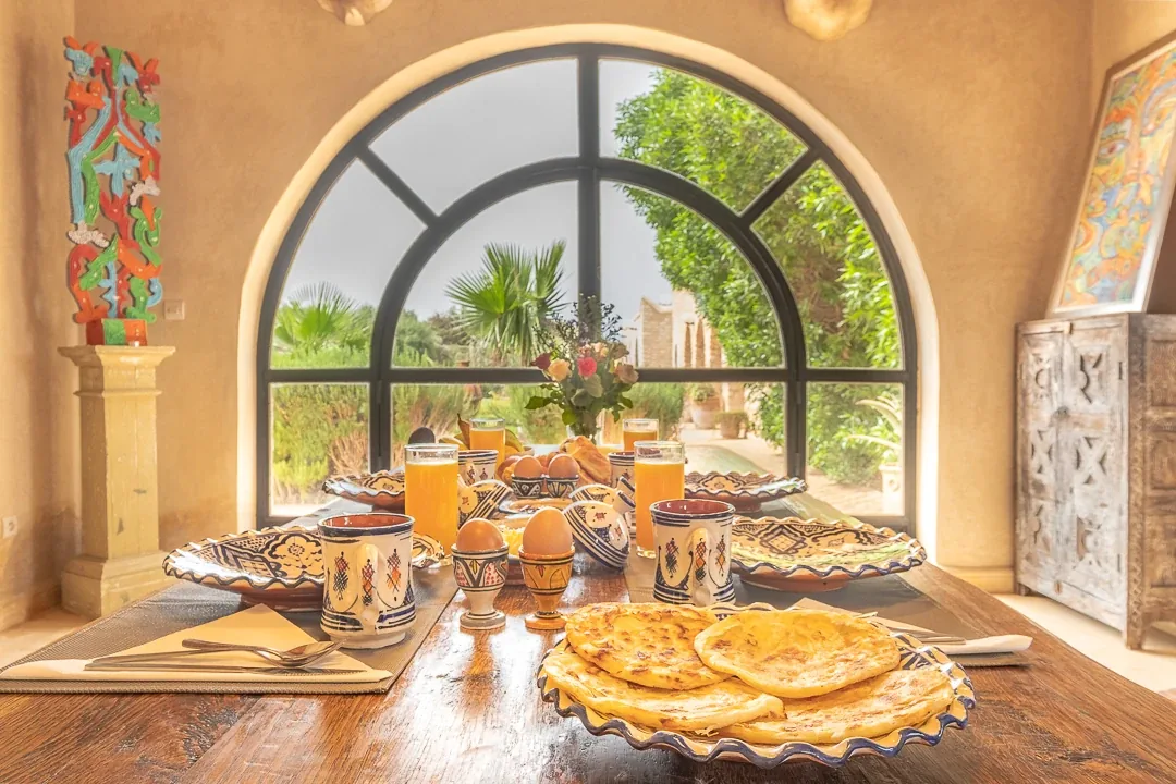 Table de petit-déjeuner dressée devant une fenêtre en arche ouverte sur la verdure