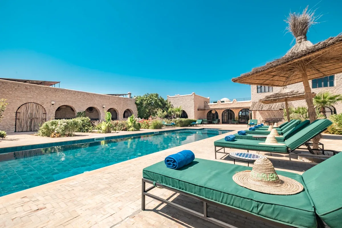 Piscine et transats devant la façade à arches de la villa, terrasse en pierre ensoleillée