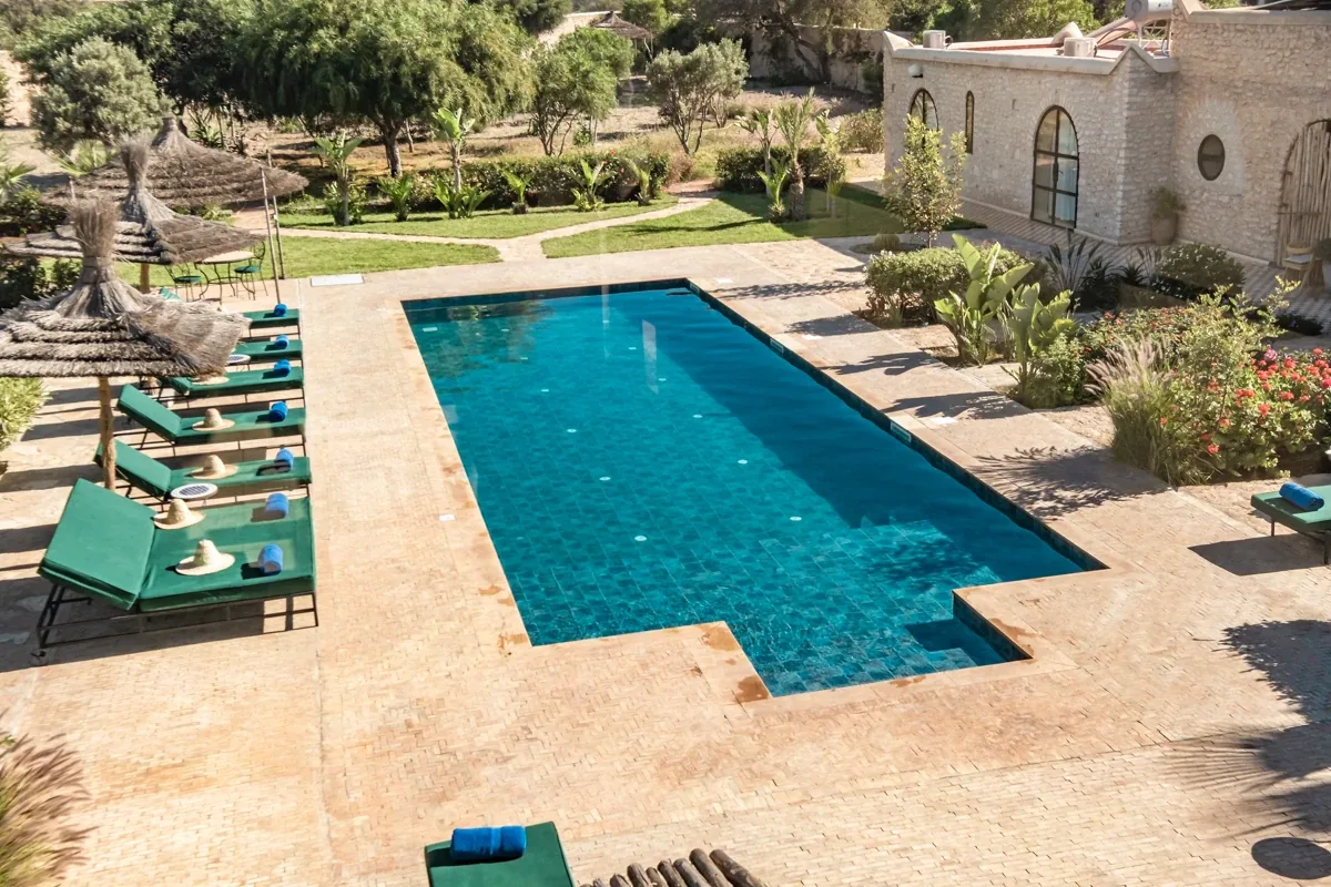 Vue plongeante sur la piscine bordée de transats et la terrasse en pierre de la villa