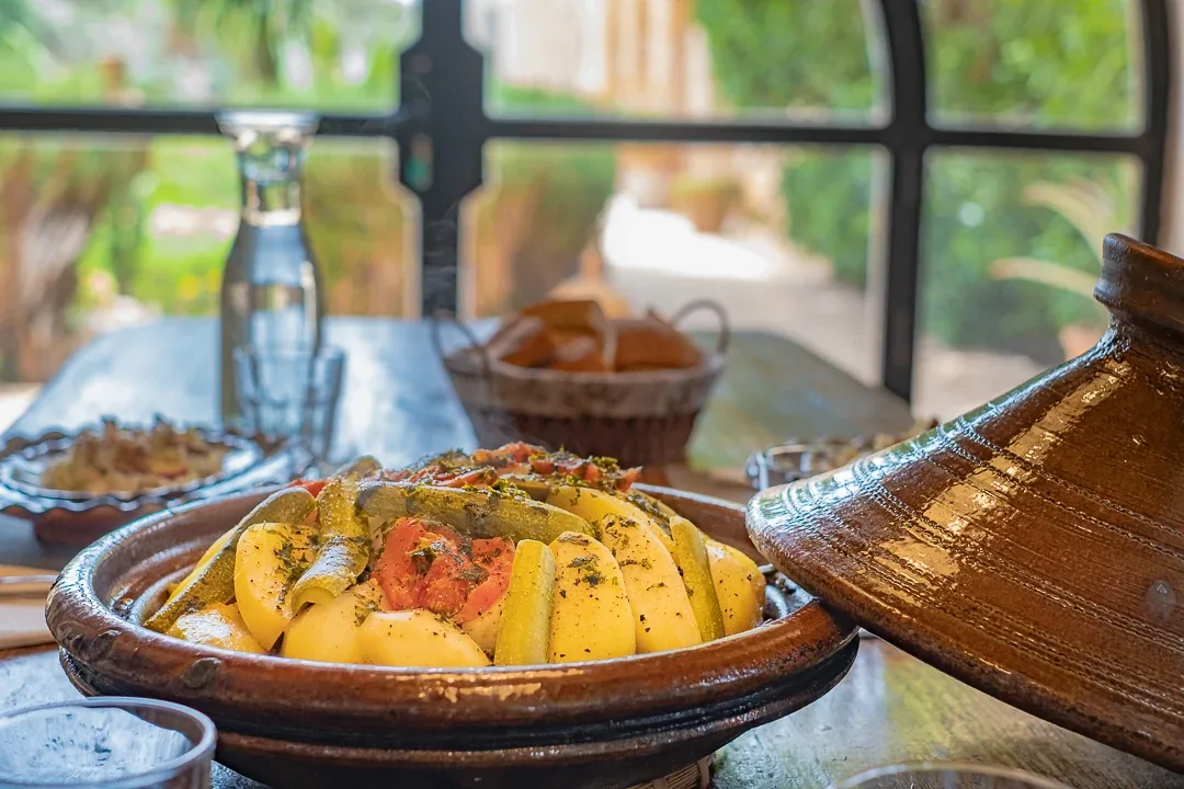 Tajine de légumes fait maison servi dans son plat en terre cuite devant une fenêtre