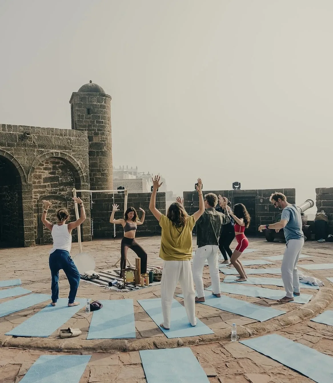 Cours de yoga collectif au lever du jour sur une terrasse face aux remparts historiques d'Essaouira