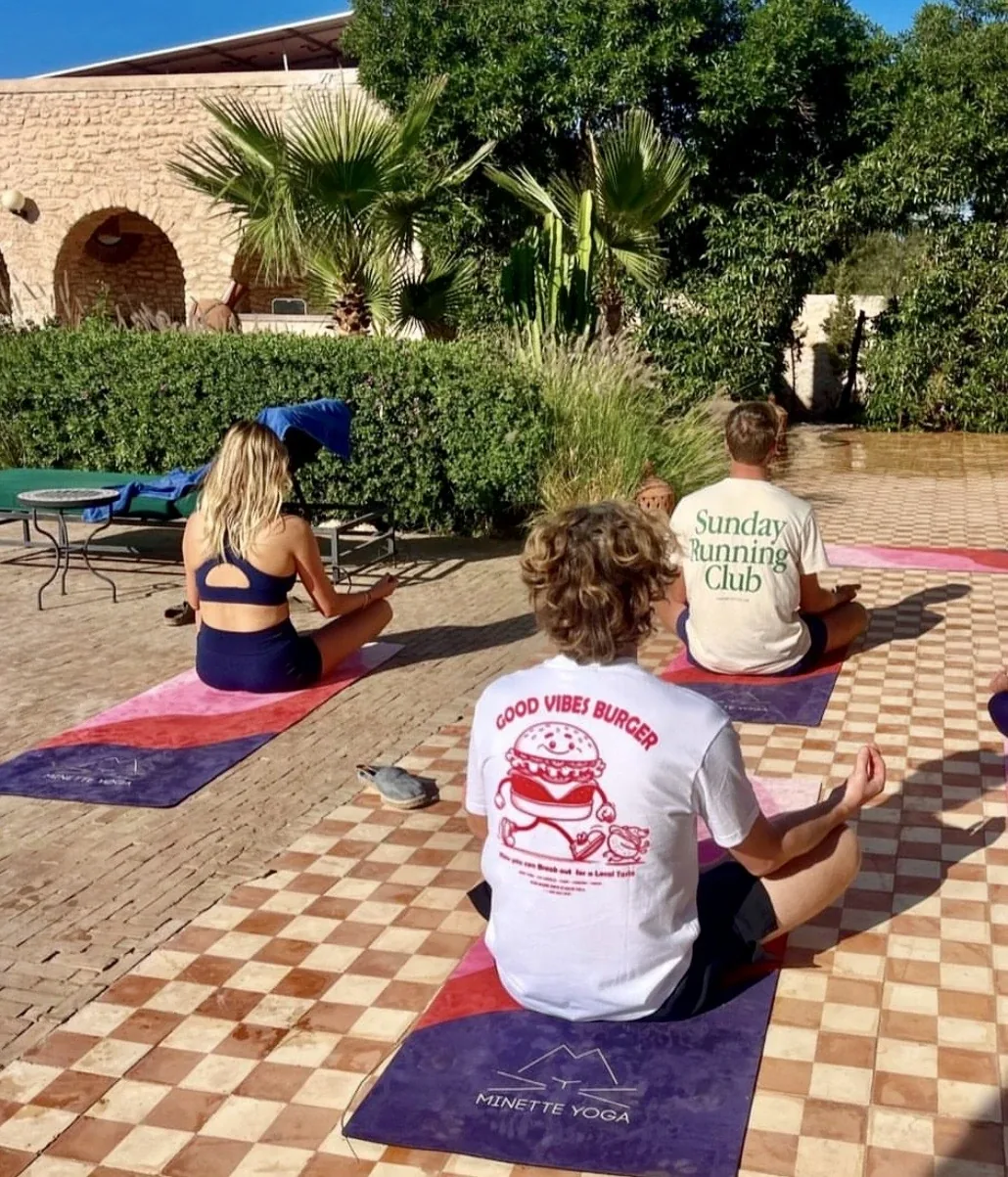 Cours de yoga en groupe en méditation assise sur tapis, sur une terrasse entourée de jardin