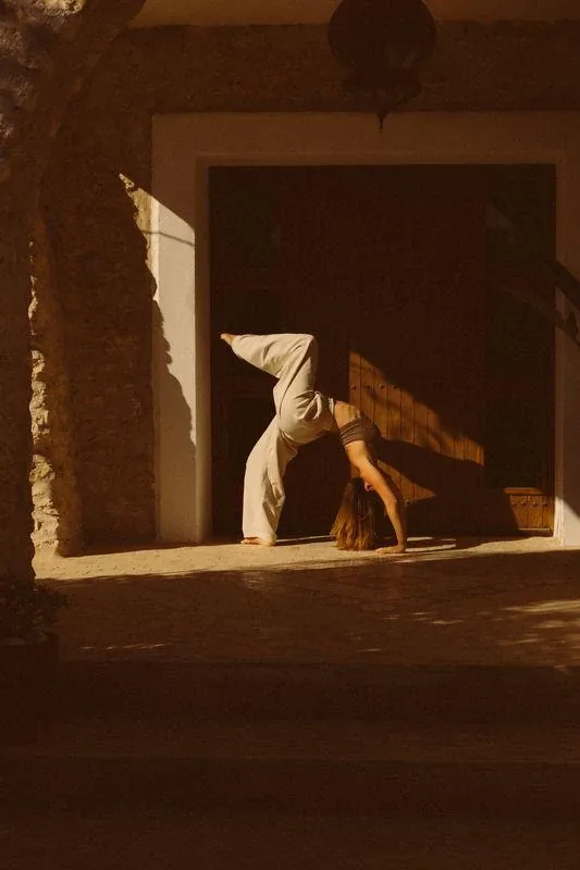 Femme réalisant une posture de yoga en pont sur un patio baigné de lumière dorée